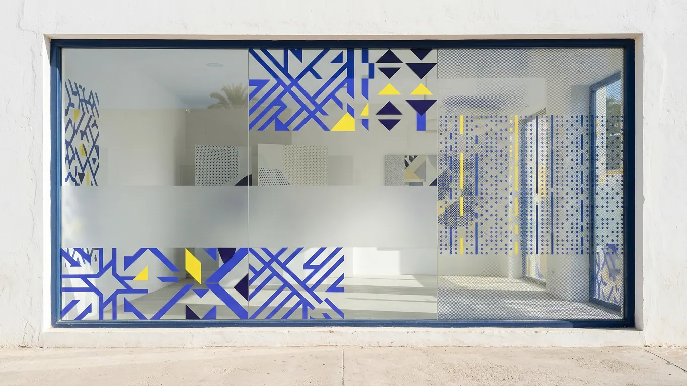 Vitrine décorée d'adhésifs découpés géométriques bleus et jaunes, d'une bande dépolie et d'un film micro-perforé — Vitrophanie et habillage de vitrine